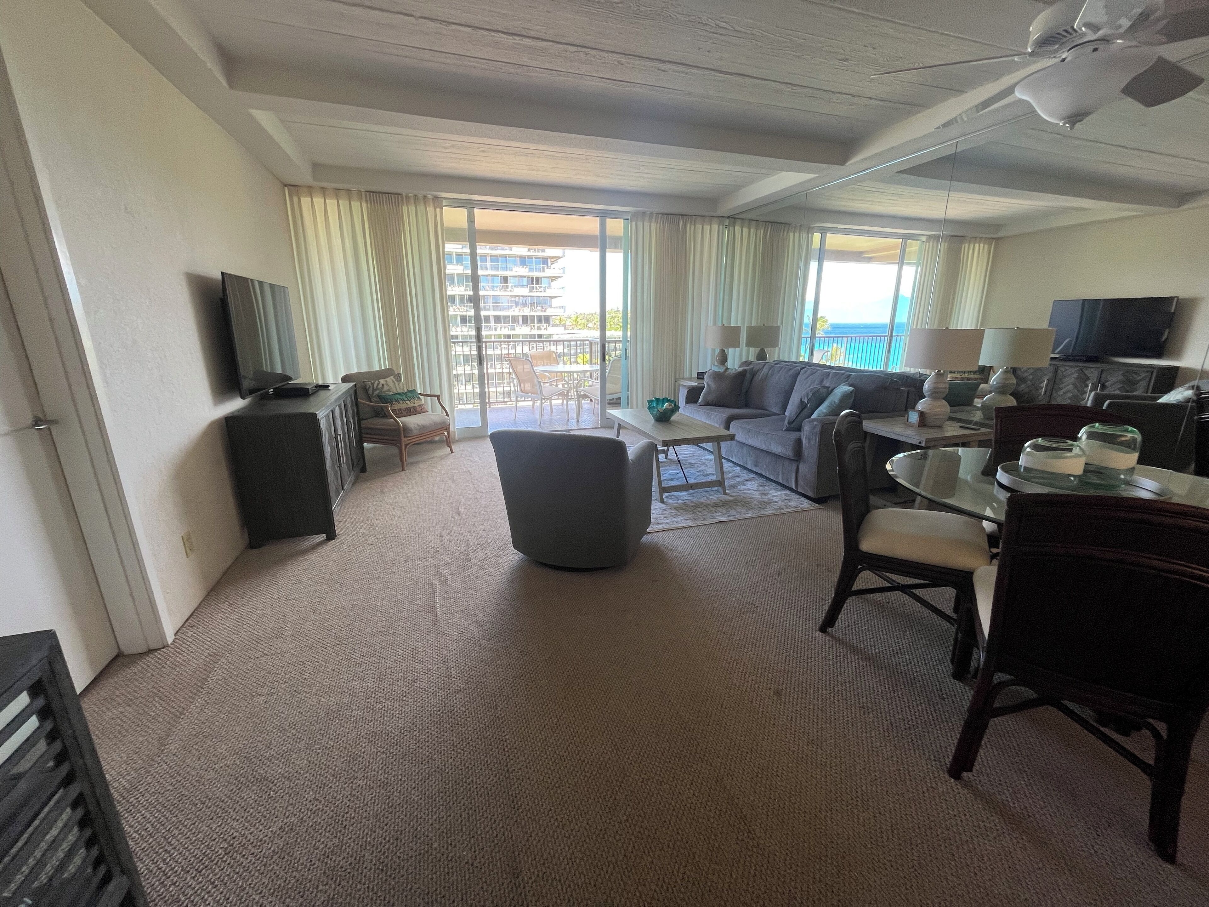 Quarto de hotel com varanda, sofá, mesa de jantar e televisão.