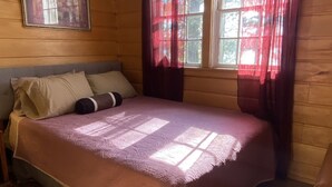 Una habitación con paneles de madera, una cama, un cuadro en la pared y una ventana con cortinas rojas.