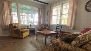 Una sala de estar con piso de madera, un sofá, una silla, una mesa y una lámpara.