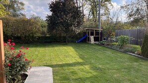 Ein Garten mit einem hölzernen Spielhäuschen, einer blauen Rutsche und einem gepflegten Rasen.