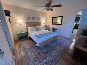 A bedroom with a bed, nightstands, a ceiling fan, a rug, and a mirror on the wall.