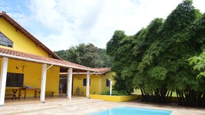 Un bâtiment jaune doté d’une piscine, d’un patio couvert et entouré de verdure.
