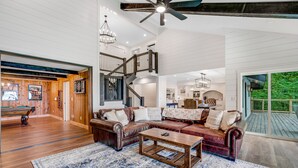 A spacious living area with a large sectional sofa, a coffee table, and a patterned rug. A staircase with a wooden railing leads to an upper level. - Mountain-view home with high-speed WiFi, wood fireplace, W/D & central AC (Beech Mountain)