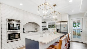 A modern kitchen with white brick walls, stainless steel appliances, a large island with bar stools, and pendant lighting. - Mountain-view home with high-speed WiFi, wood fireplace, W/D & central AC (Beech Mountain)