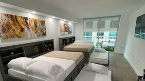 Ein modernes Hotelzimmer mit drei Betten, einem großen Fenster und Bildern an den Wänden.