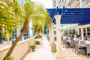Relax on the poolside terrace surrounded by palm trees and lounge under the shade of a blue awning.