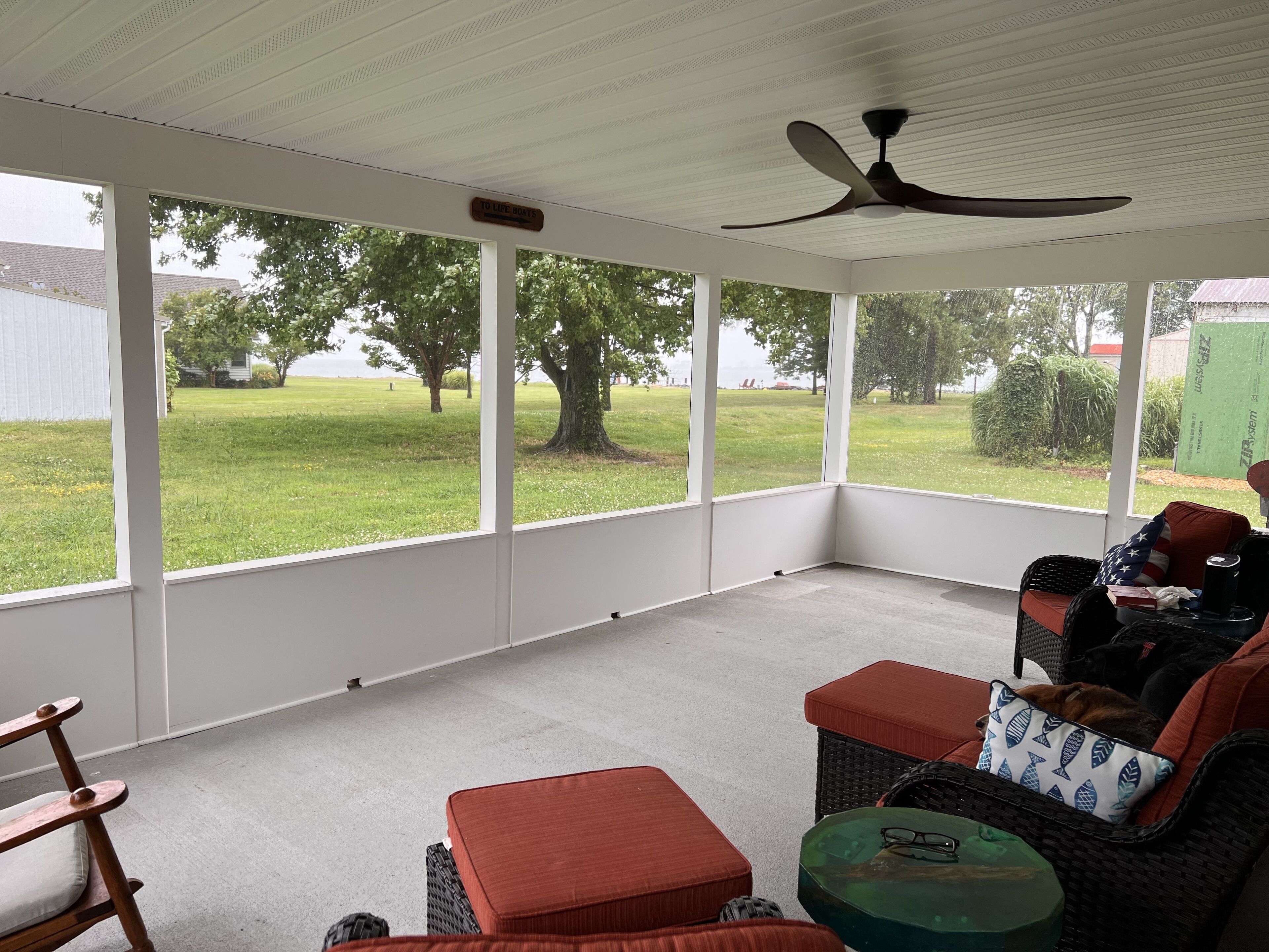 A covered patio area with a ceiling fan, wicker furniture, and a view of a grassy yard with trees.