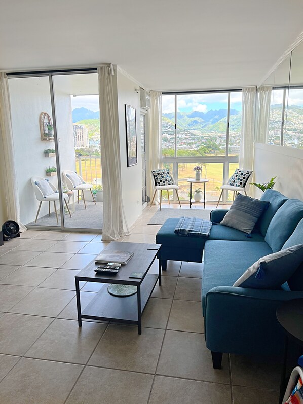 Amplia sala de estar con un sofá azul, una mesa de centro y un balcón con vistas a la ciudad y las montañas.