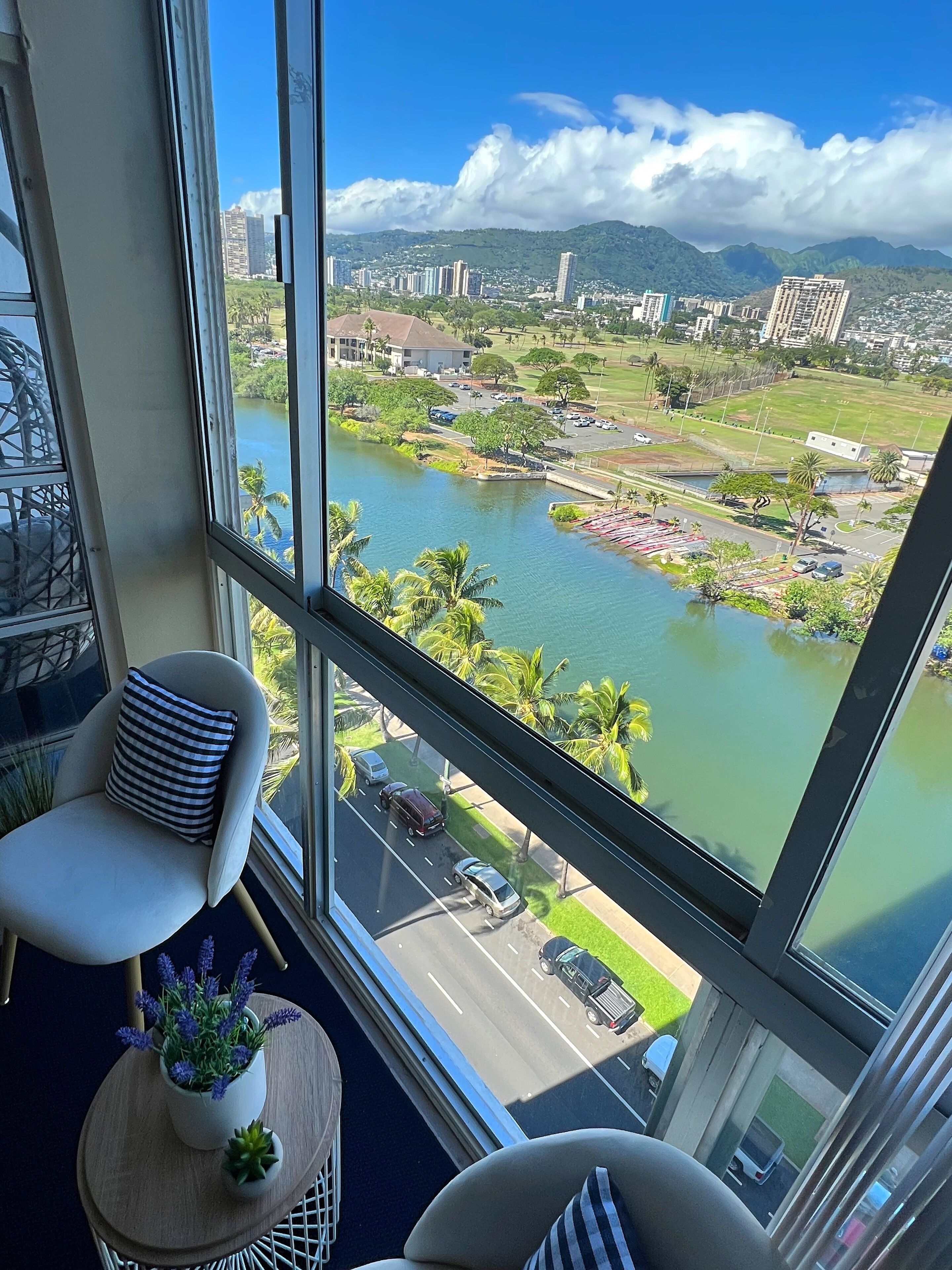 Habitación en un rascacielos con un amplio ventanal que ofrece vistas a un paisaje urbano, un río y un parque.