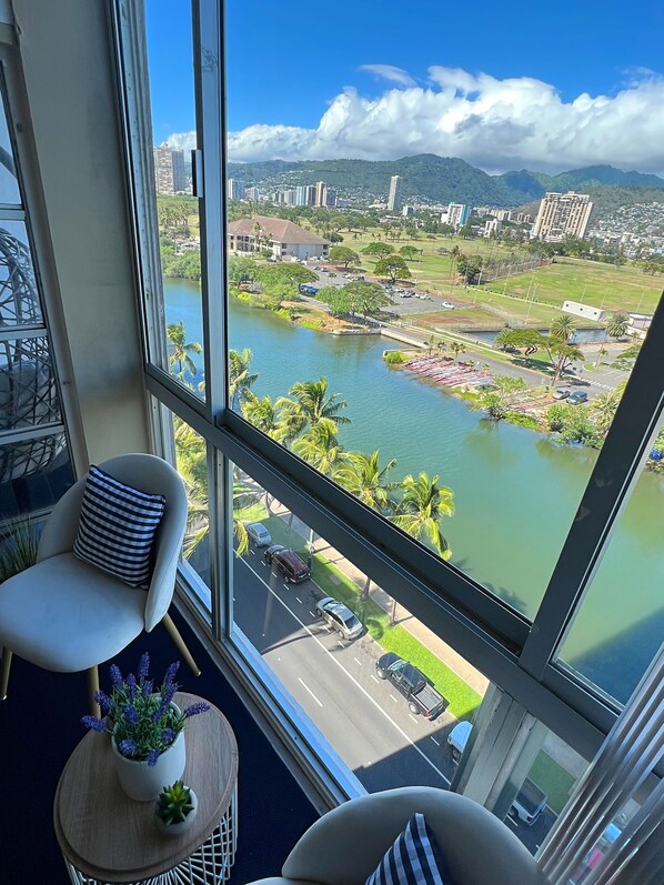 A high-rise room with a large window overlooking a cityscape, a river, and a park.