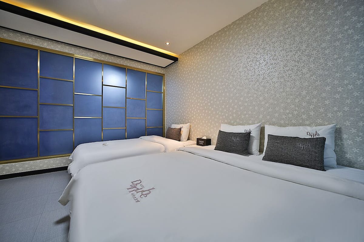 A modern hotel room with a large bed, a nightstand, and a wall with a geometric pattern.