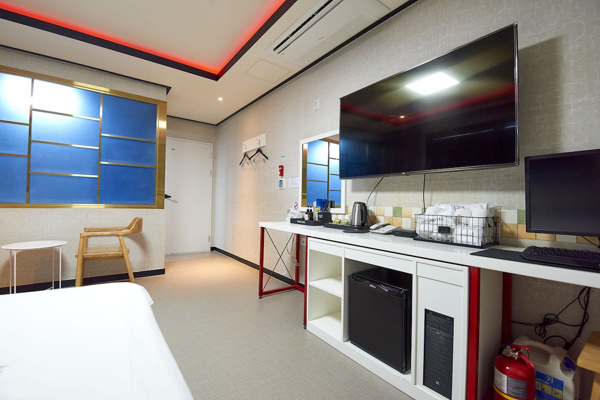 A hotel room with a bed, a desk with a computer, a TV, and a small table.