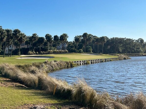 En golfbane med et vandareal, en træbro og en klar himmel.