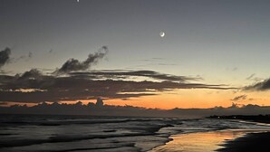 A beach scene with a crescent moon, ocean waves, and a distant shoreline. - Birdie`s Bungalow on Fripp/Cards Avail/Golf Cart (Fripp Island)