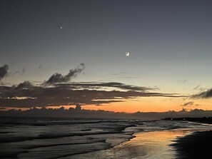 En strandscene med en halvmåne, bølger og en fjerntliggende kystlinje.