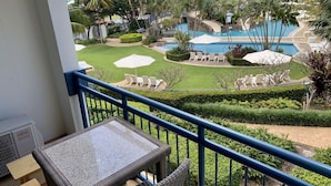 A balcony with a view of a resort pool area, including lounge chairs and umbrellas.