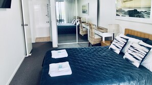 A hotel room with a large bed, a desk, a chair, and a view of the sea.