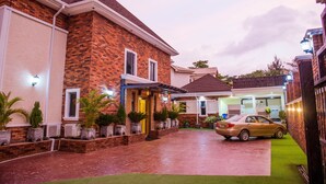 A two-story house with a brick facade, a covered driveway, and a car parked in the driveway. - Pinnatech Suites (Abuja)