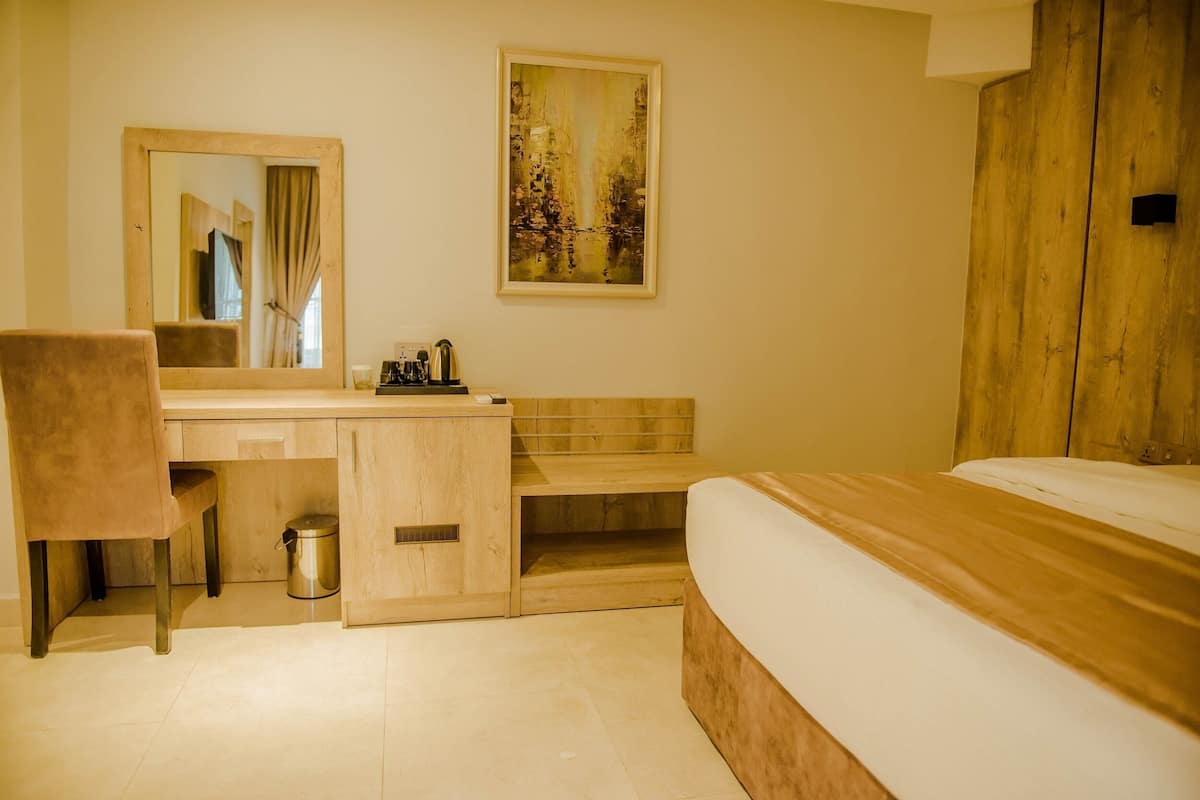 A bedroom with a wooden bed, a desk with a chair, a small trash bin, and a painting on the wall.