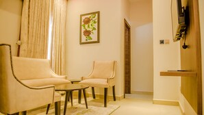 A living room with two armchairs, a small table, and a decorative wall piece. - Pinnatech Suites (Abuja)