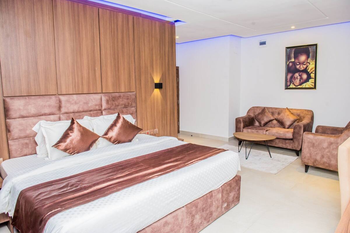 A modern bedroom with a large bed, a wooden headboard, a brown sofa, and a small table.