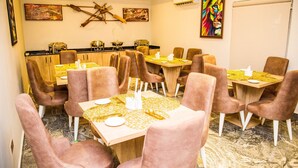 A dining area with multiple tables and chairs, equipped with table settings and a kitchen in the background. - Pinnatech Suites (Abuja)