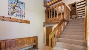 A wooden staircase with a bench at the bottom, a wooden handrail, and a poster on the wall. - Cozy Family sized Condo- access to Pools and other Summer time Amenities (Sun Valley)
