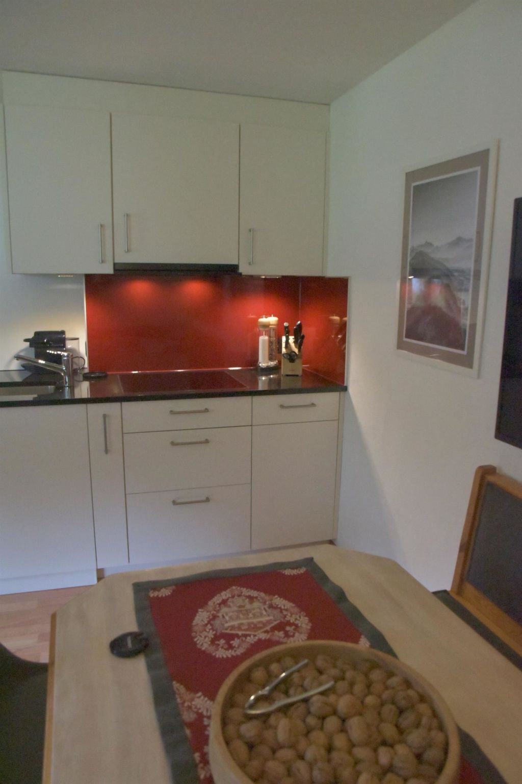 A compact kitchen with white cabinets, a red backsplash, and a dining area with a table set for two.