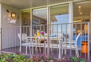 A balcony with white chairs and a table, a glass door, and a view of the interior.