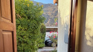 Eine Holztür, die zu einer Auffahrt mit Fußmatte, einem Auto und einem Berg im Hintergrund führt.