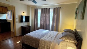 Ein Schlafzimmer mit einem Bett, einem Deckenventilator, einem Fernseher und einem Fenster mit Vorhängen.
