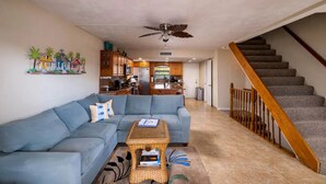 A living room with a blue sectional sofa, a small coffee table, and a staircase with wooden railings. - Free Golf Cart Free Kayaks Steps to Pool Pickleball (Key Largo)