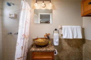 Une salle de bain avec un lavabo en forme de bol en verre, une douche avec un rideau, un miroir et un porte-serviettes.