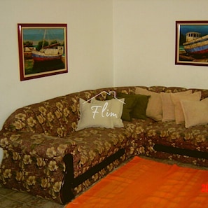 Un salón con sofá floral, un cuadro de un barco en la pared y un cojín con la palabra "Flim".