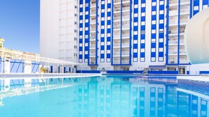 Une piscine à l’eau d’un bleu cristallin, entourée d’un bâtiment aux rayures verticales bleues et blanches et doté de balcons.