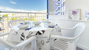 Un balcon avec une table dressée pour deux personnes, des chaises blanches et une vue sur les bâtiments en arrière-plan.