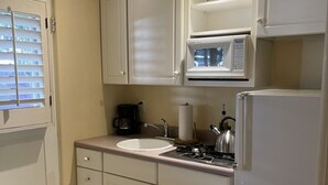 A compact kitchen with white cabinets, a microwave, a stove, and a sink.