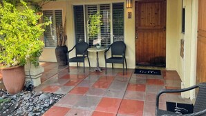 A patio with two chairs and a table, a potted plant, and a wooden door.