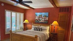 A bedroom with a wooden bed, two bedside lamps, a ceiling fan, a window with blinds, and a painting on the wall. - Room 4️⃣- a beautiful studio in boutique hotel,  a few steps from Downtown PS 🌺 (Palm Springs)