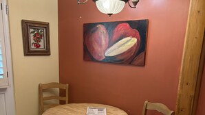 A dining area with a round wooden table, two chairs, a chandelier, a painting of fruit, and a welcome sign. - Room 4️⃣- a beautiful studio in boutique hotel,  a few steps from Downtown PS 🌺 (Palm Springs)