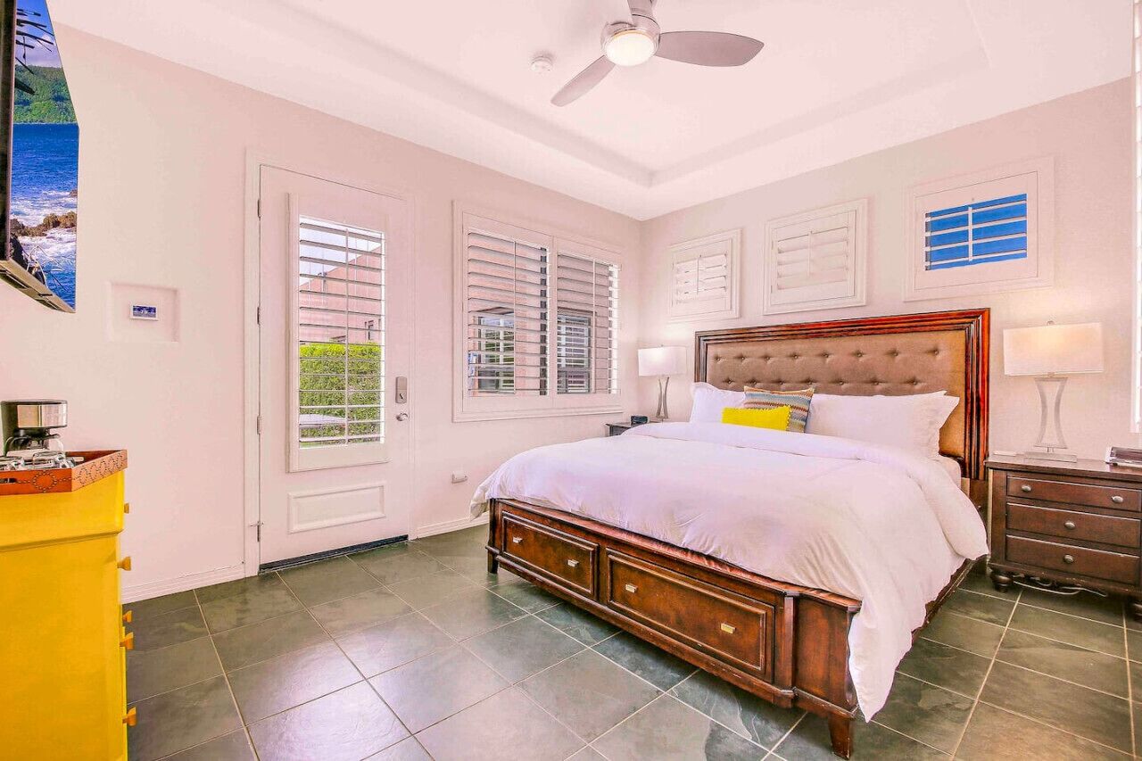 A bedroom with a large bed, a ceiling fan, and a window with blinds.