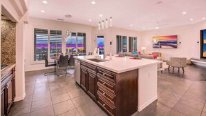 A spacious kitchen with a large island, modern appliances, and a dining area with chairs and a table. - THE MASTERPIECE- Half Acre-8BR-5.5BA (Indio)