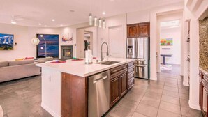 A modern kitchen with a central island, stainless steel appliances, and a dining area with a sofa and artwork. - THE MASTERPIECE- Half Acre-8BR-5.5BA (Indio)