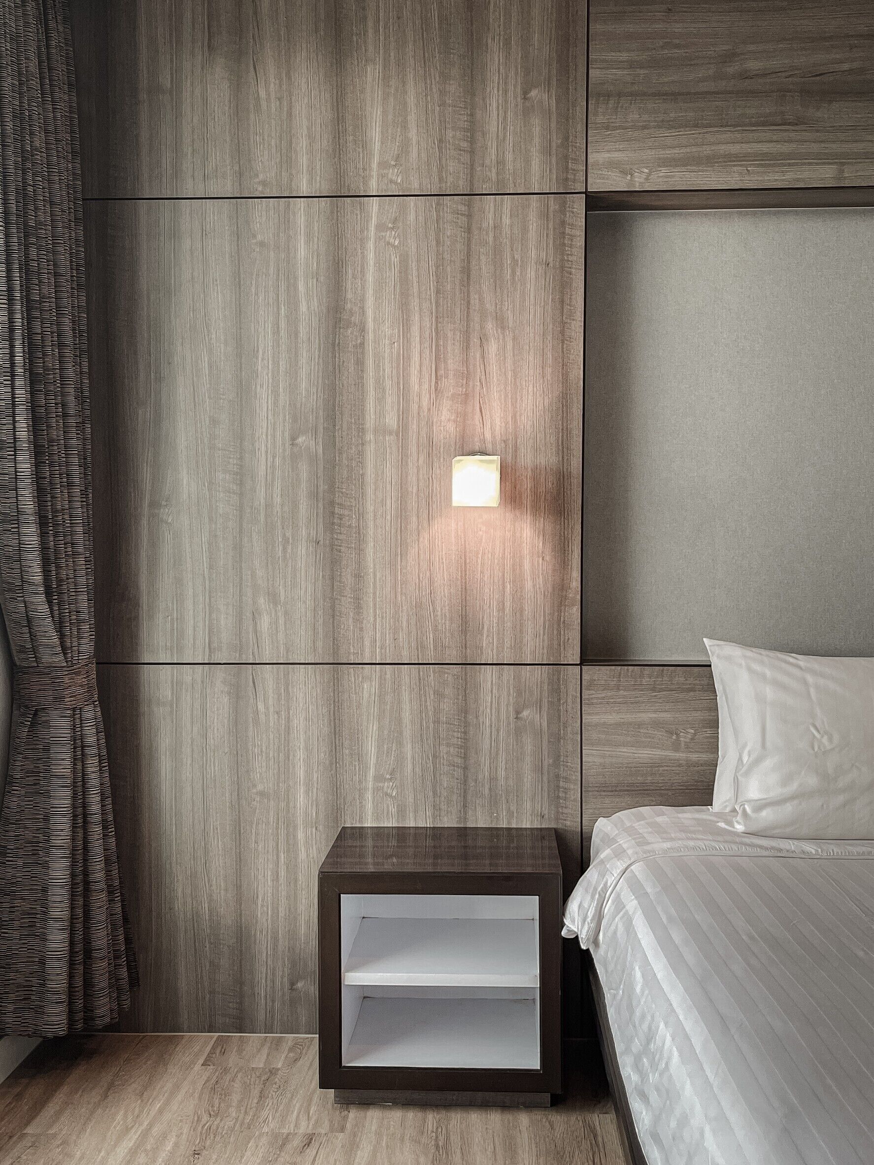 Camera da letto moderna con testiera in legno, comodino con ripiano integrato e lampada a parete.