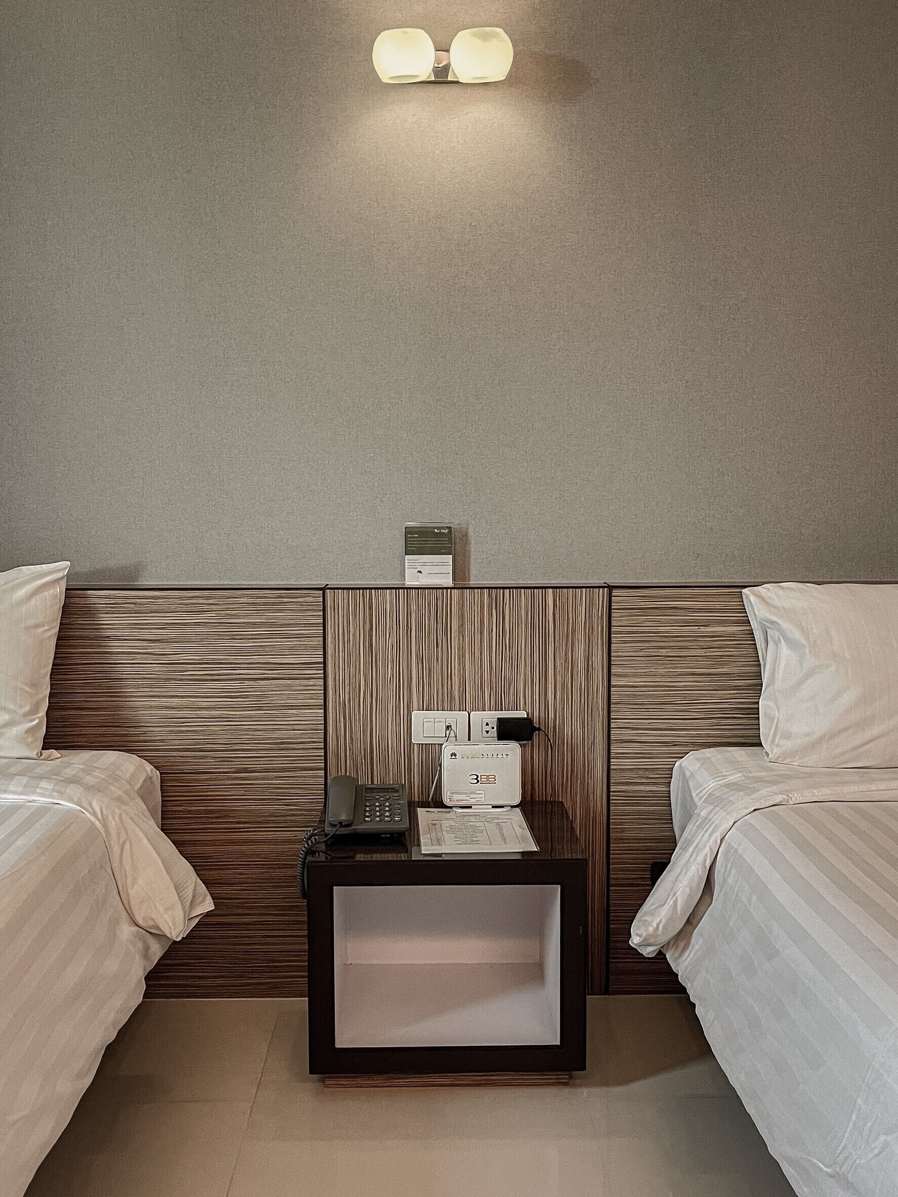Habitación de hotel con dos camas, una mesita de noche con teléfono y una pequeña mesa, y una lámpara de pared.