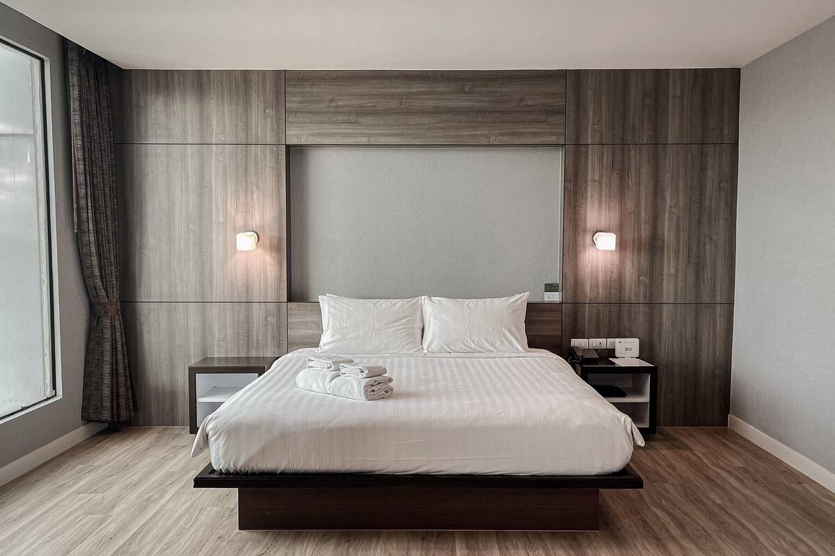 Un dormitorio moderno con una cama grande, cabecera de madera, mesitas de noche y una ventana con cortinas.