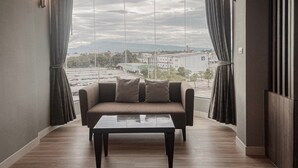 Uma sala de estar moderna com um sofá e uma mesa de centro, janelas amplas com cortinas e vista para um horizonte urbano.
