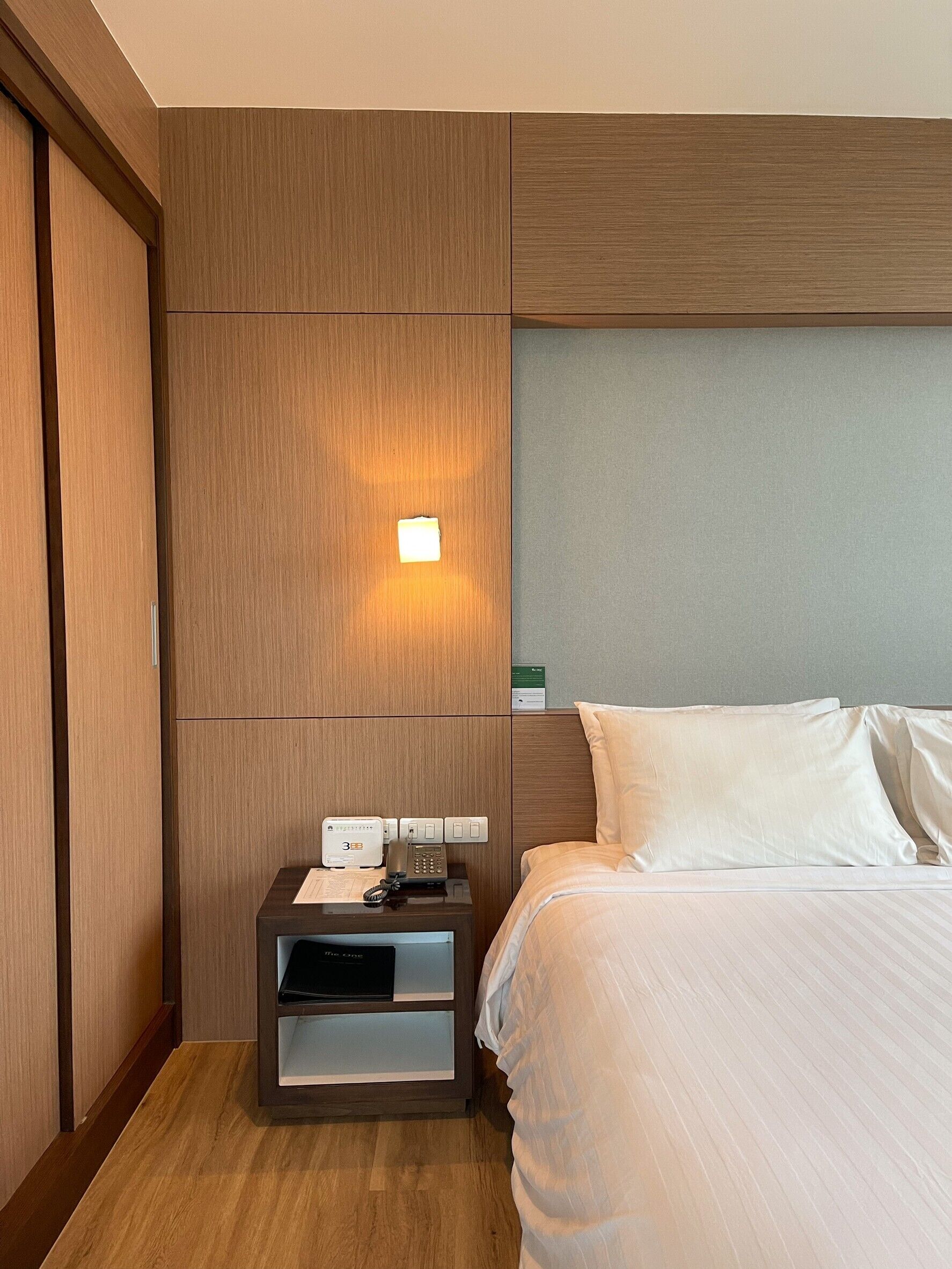 Une chambre d’hôtel avec un lit, une table de chevet avec un téléphone et une lampe, et une armoire en bois.