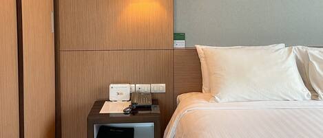 Une chambre d’hôtel avec un lit, une table de chevet avec un téléphone et une lampe, et une armoire en bois.