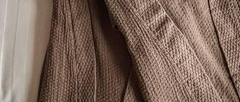A bed with a white sheet and a brown knitted garment folded on it.